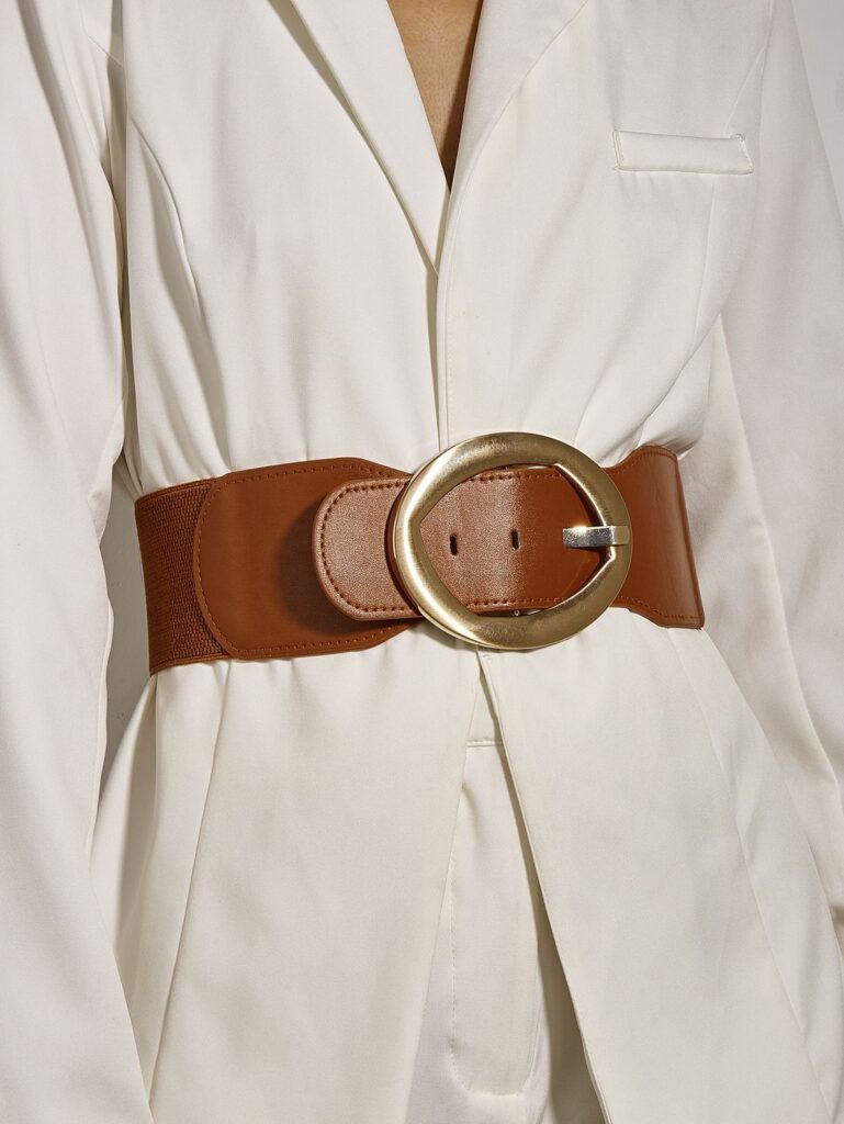 A stylish lady wearing a white blazer cinched at the waist with a bold brown leather belt.