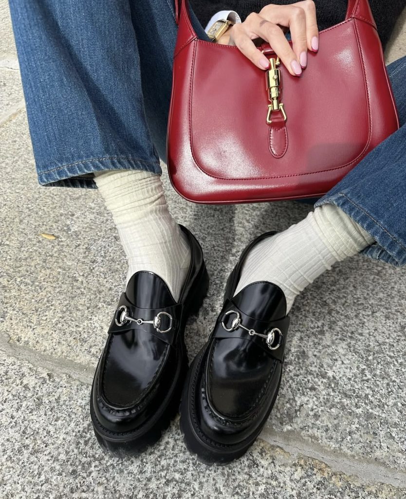 A pair of black loafers with a cute red bag in the background