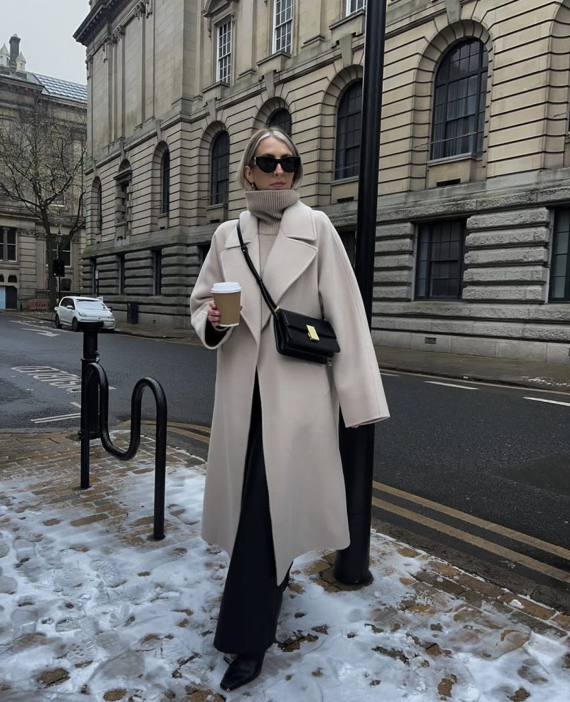 A beautiful white lady wearing a beige colored statement coat