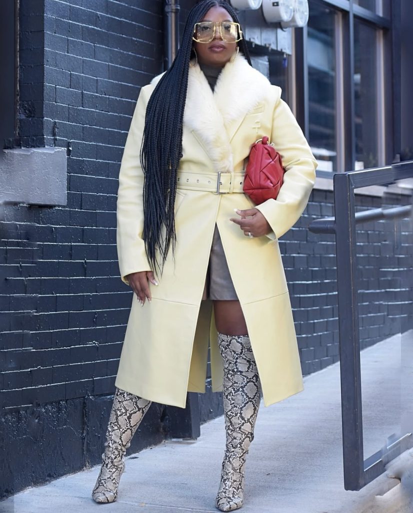 A black lady looking very classy and chic in a cream colored statement coat