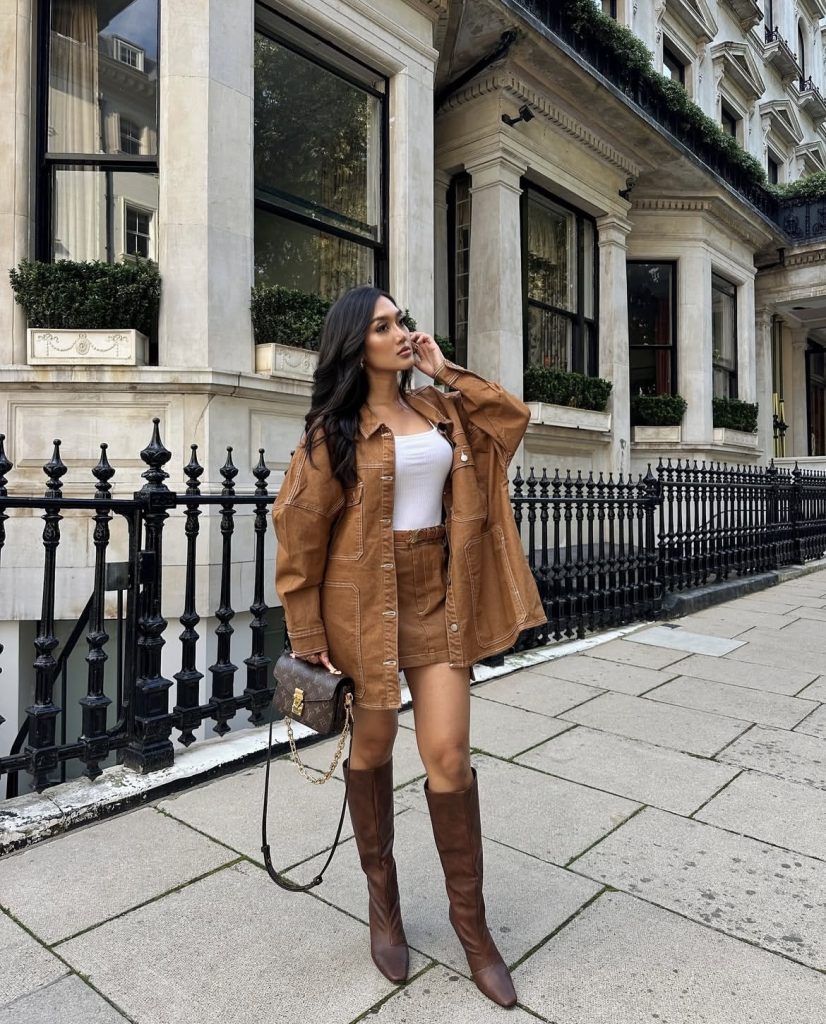 A beautiful lady wearing a brown monochromatic outfit with brown long boots and brown purse