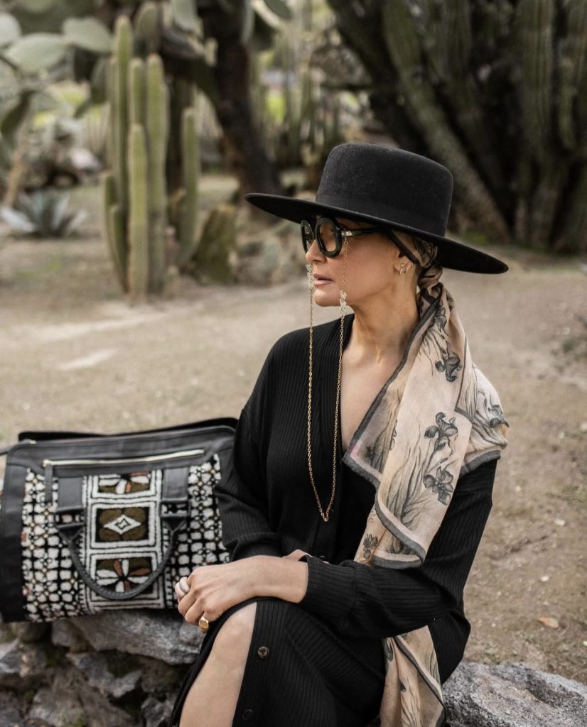 A beautiful lady wearing an all black outfit with a hat, scarf and sunglasses