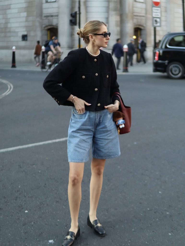 A beautiful woman dressed in casual baggy blue jeans shorts and black twill cropped blazer with a red handbag.